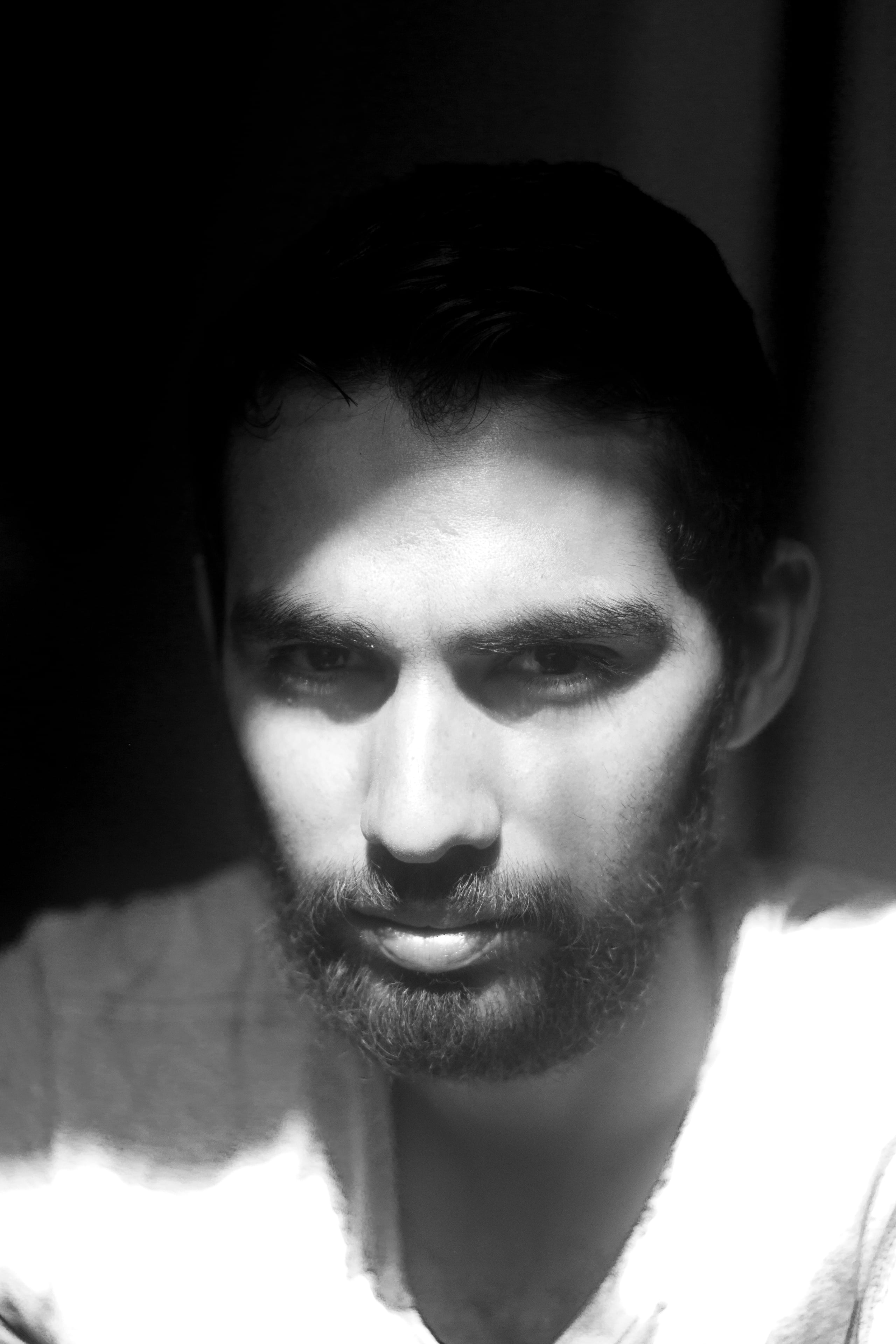 High contrast black and white portrait emphasizing dramatic split lighting and shadow patterns across the subject's face