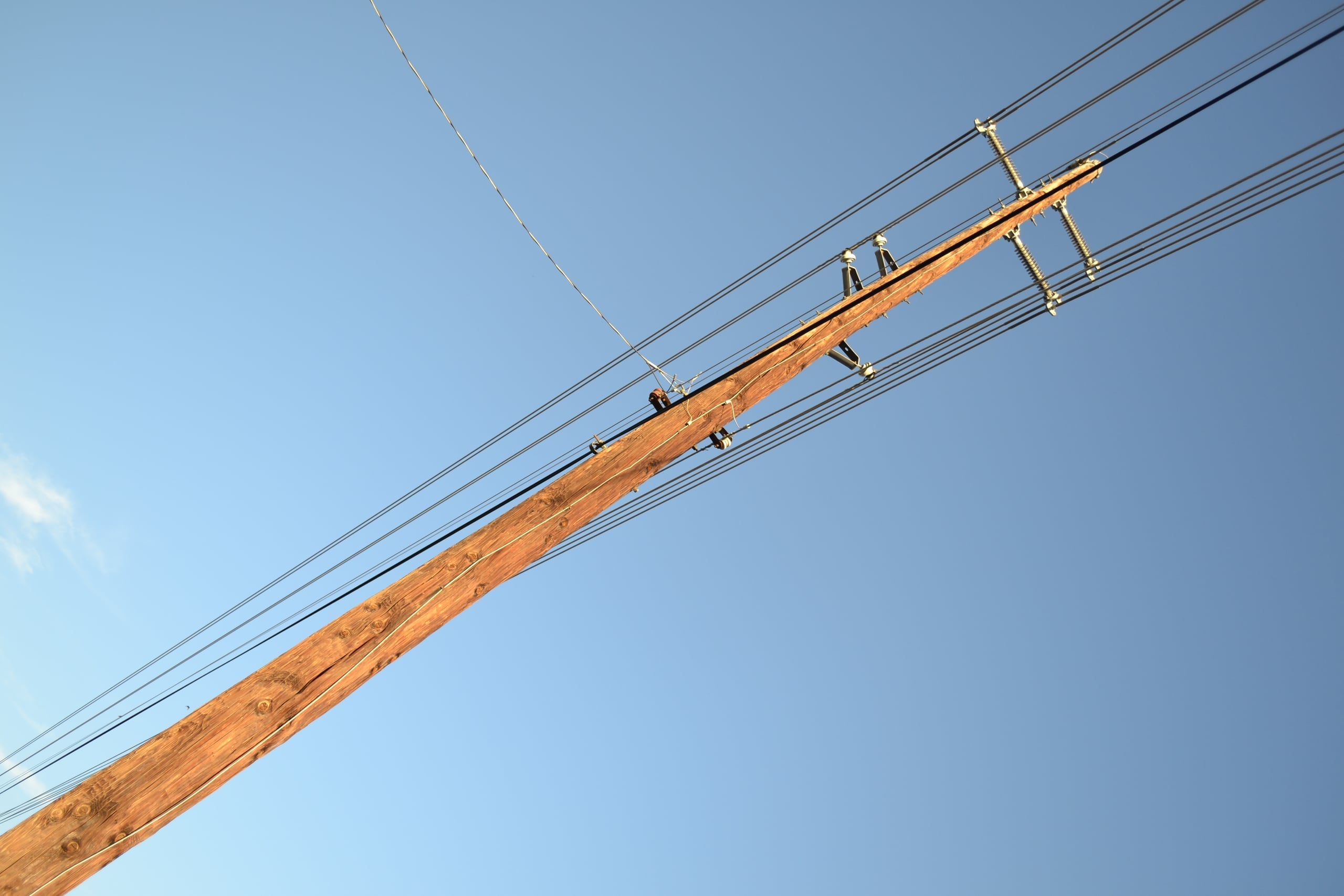 Low angle photograph of a wooden power pole with crossbeam and multiple power lines stretching diagonally across a gradient blue sky at golden hour