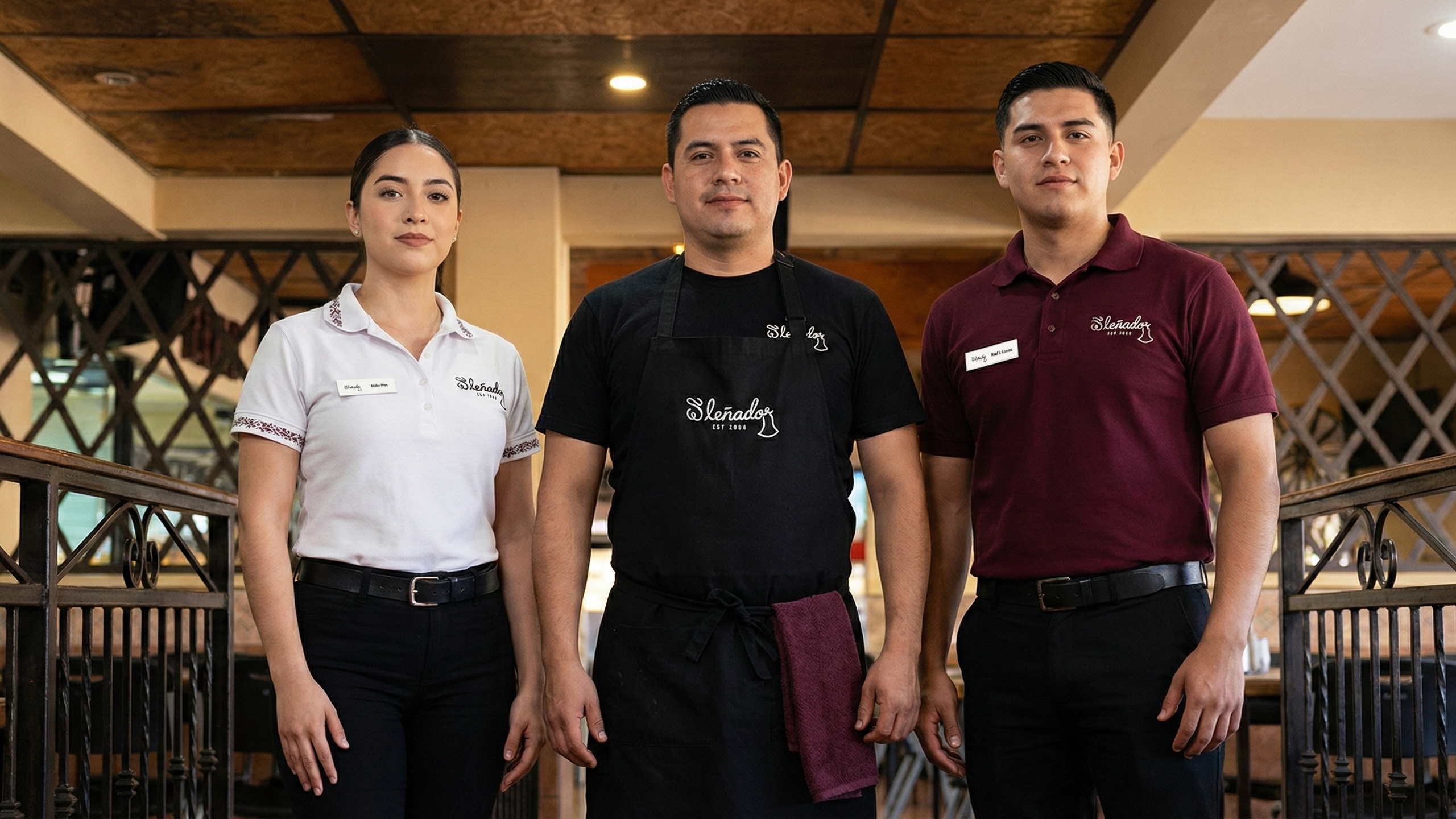 Three El Lenador restaurant staff members posing in white, black, and maroon uniforms with embroidered cursive logos