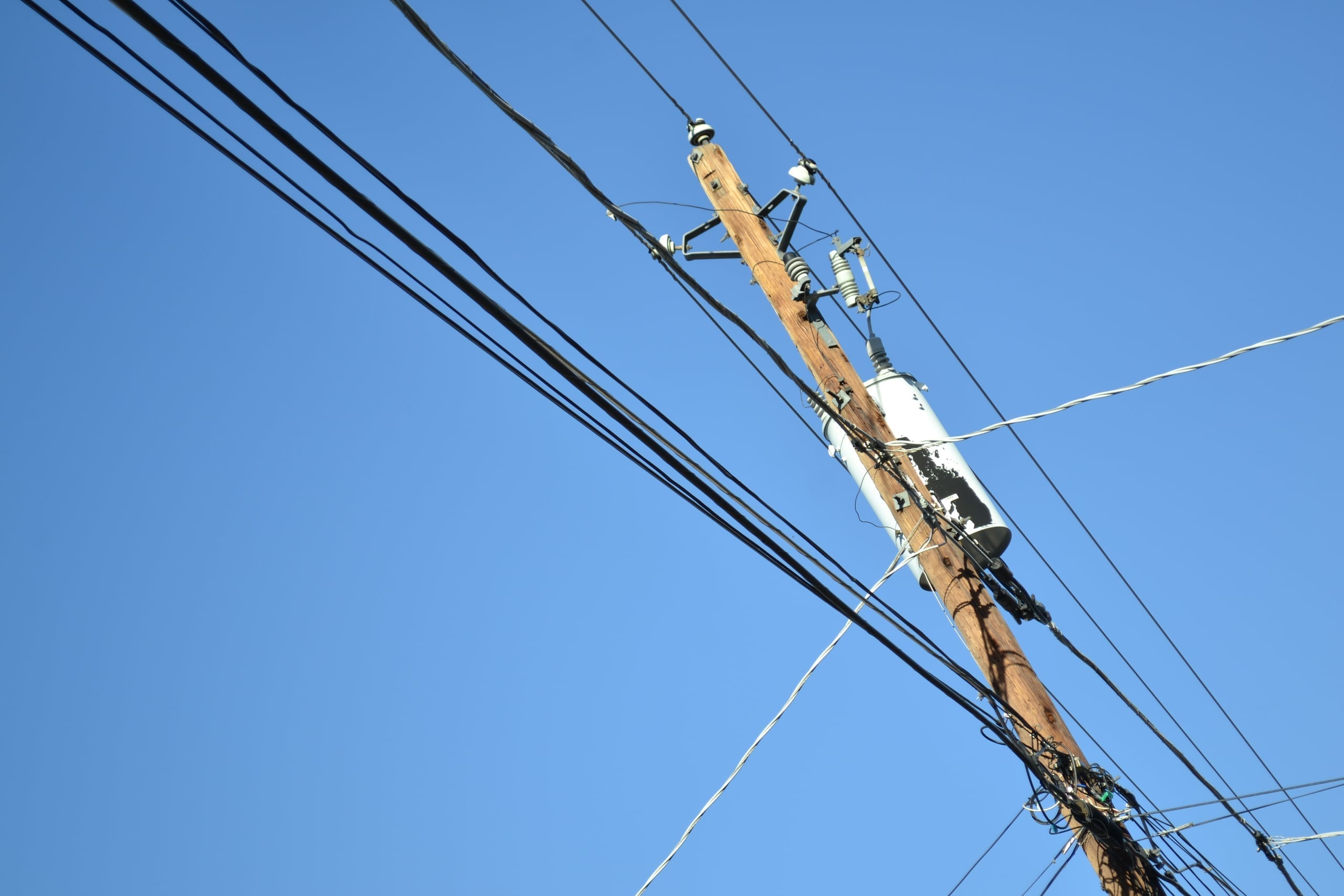 Diagonal composition of a wooden utility pole with power lines and transformer against a clear deep blue sky