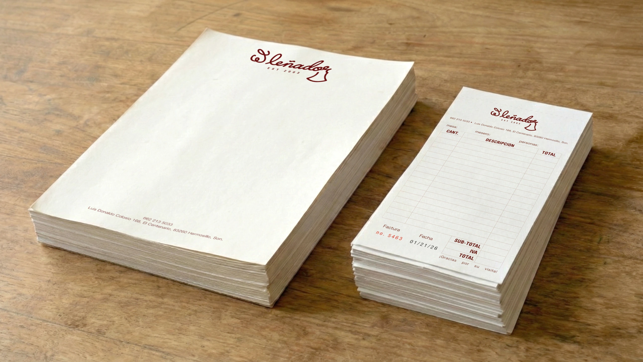Stack of cream-colored branded letterhead and invoice pads on wooden surface featuring El Lenador maroon cursive logo header with contact details and ruled form layout for restaurant orders