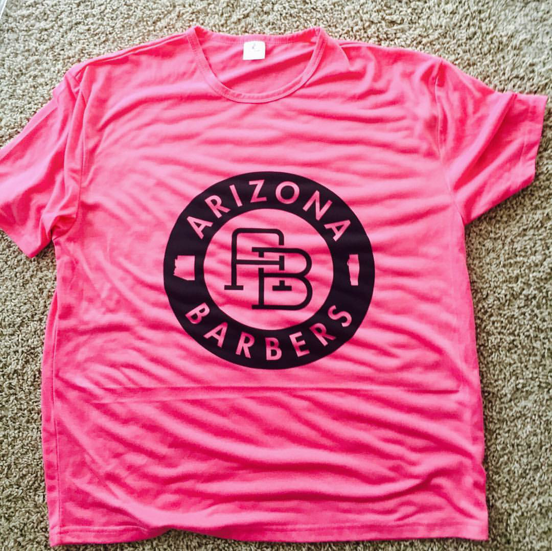 Hot pink t-shirt featuring circular Arizona Barbers badge logo with AB monogram center