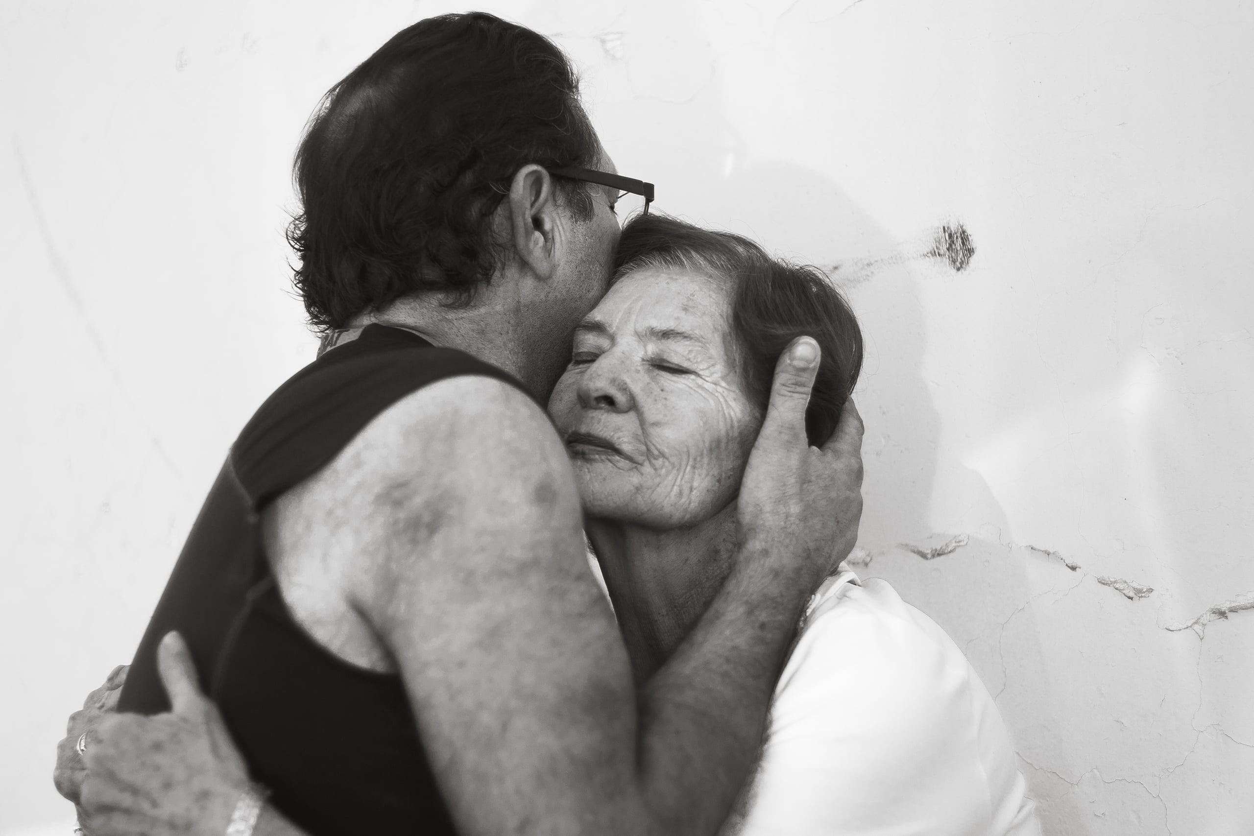 Emotional black and white photograph of an older couple in tender embrace, the man kissing the woman's forehead while cradling her face