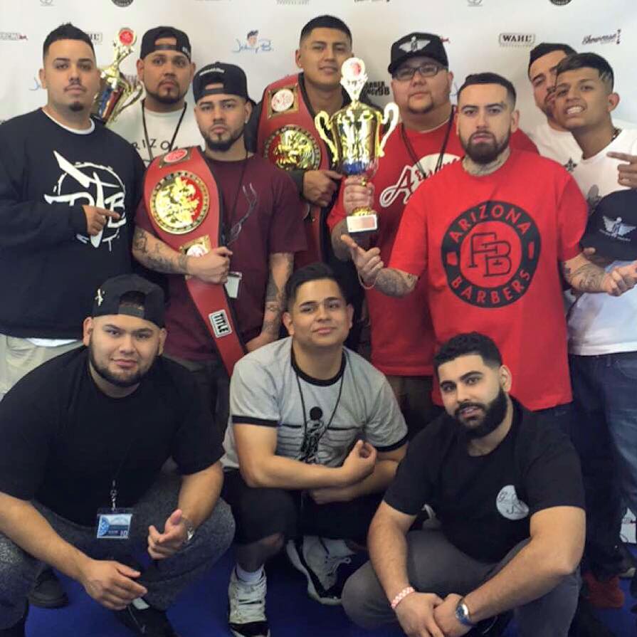 Group photo of Arizona Barbers team at barber competition holding championship belts and trophies wearing branded apparel