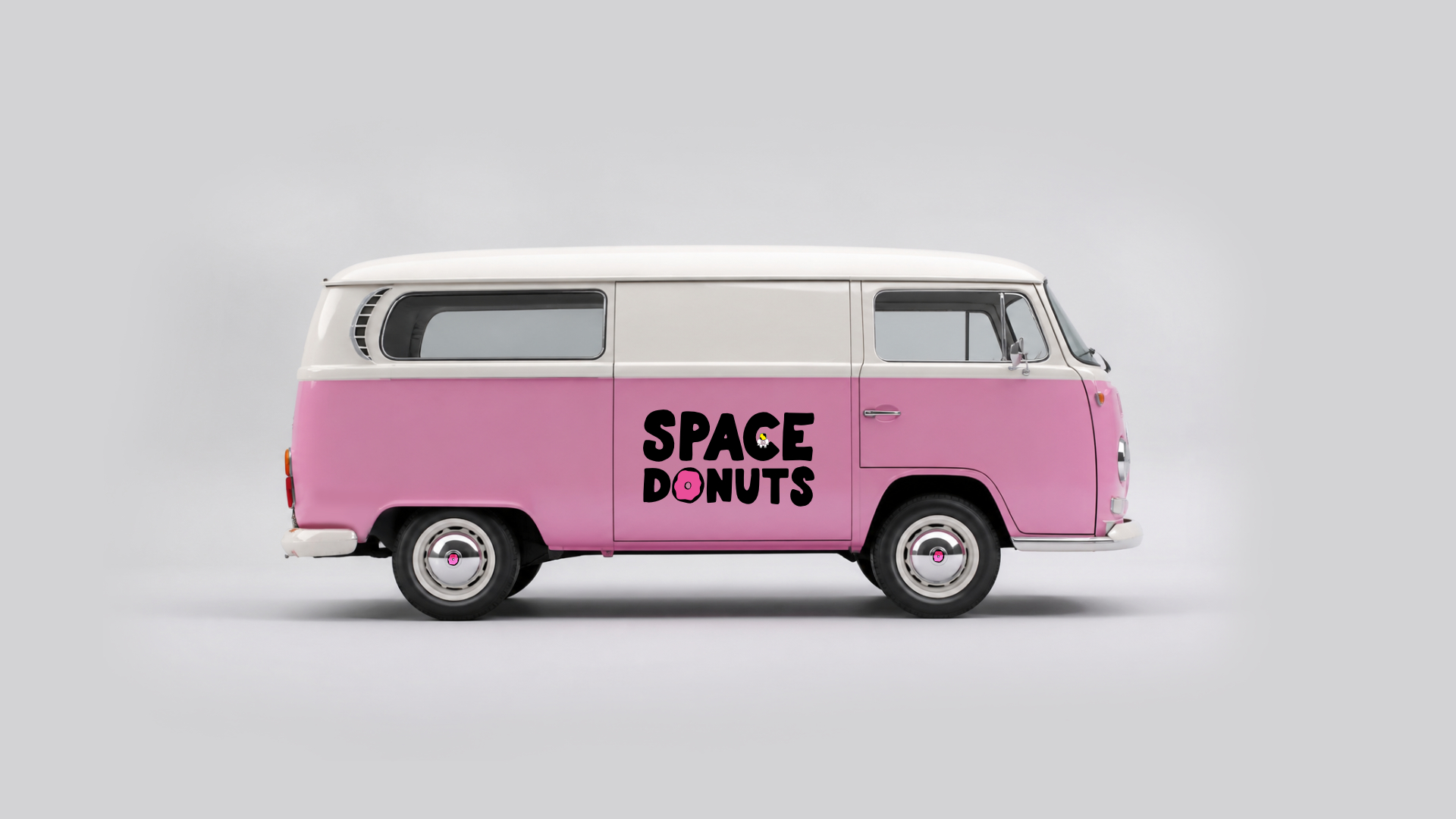 Side view of a vintage Volkswagen Type 2 van in dusty pink color with the Space Donuts logo featuring the pink donut O displayed on the side door panel, photographed on a neutral gray background