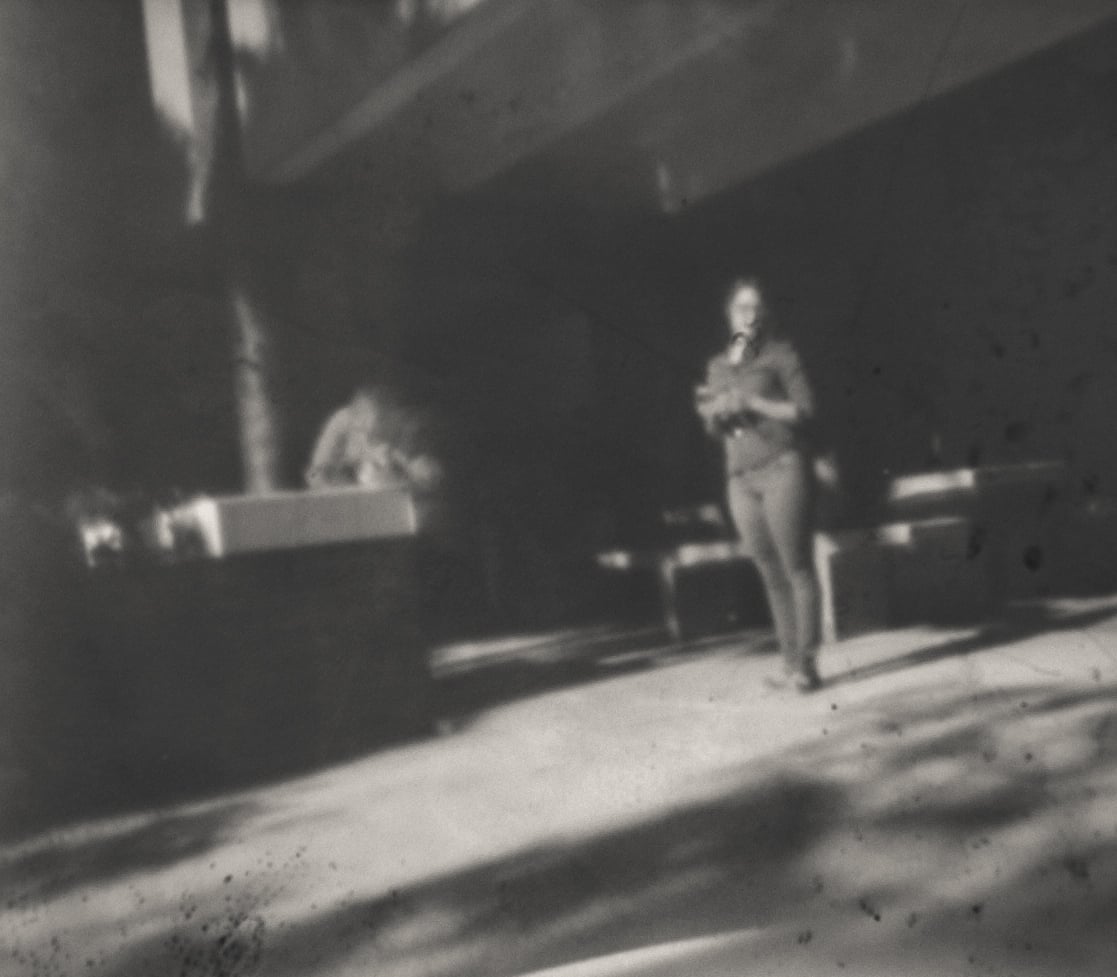 Soft focus black and white photograph of a solitary figure standing in a bright outdoor space, creating an ethereal dreamy atmosphere