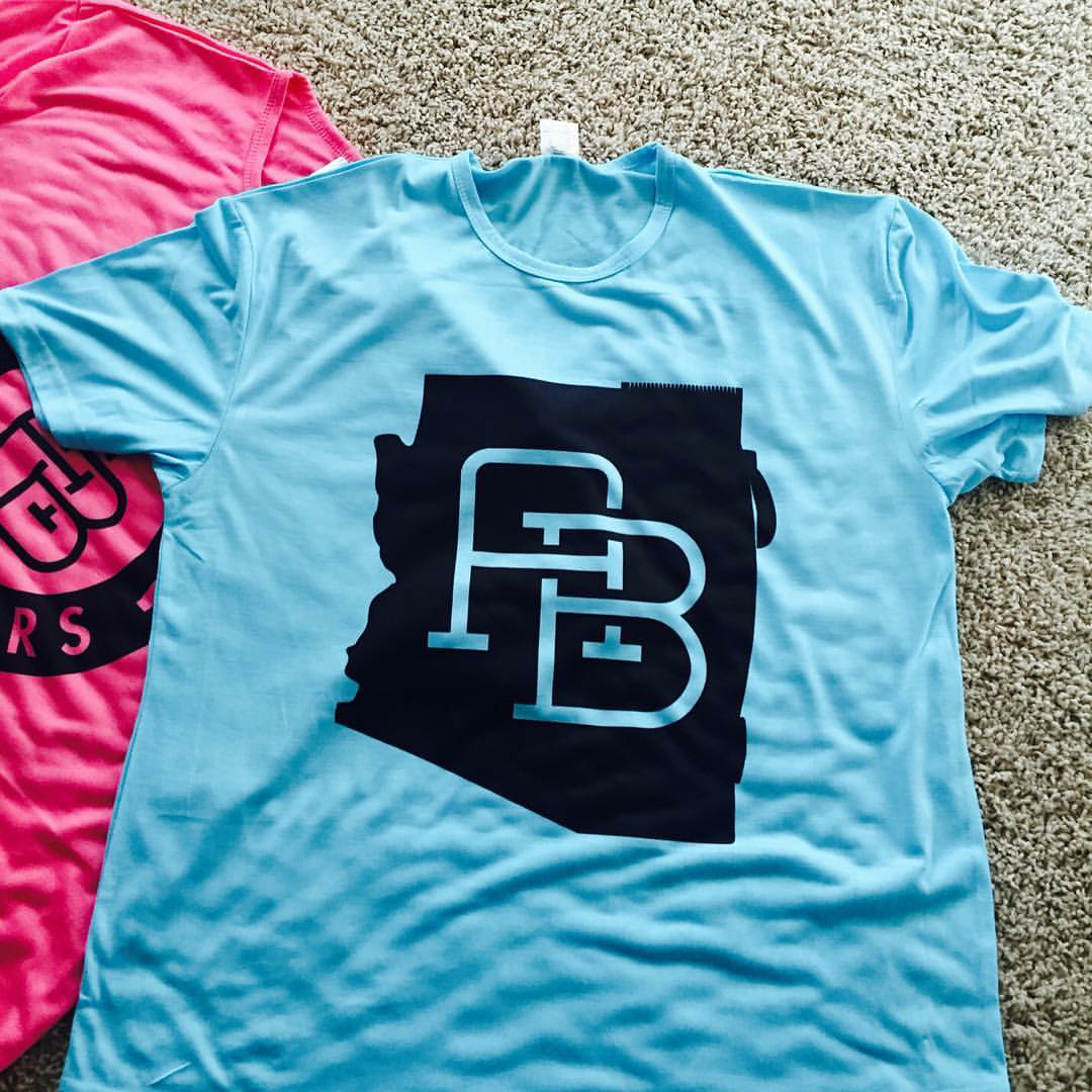 Light blue t-shirt with black Arizona state silhouette and AB monogram next to pink branded shirt