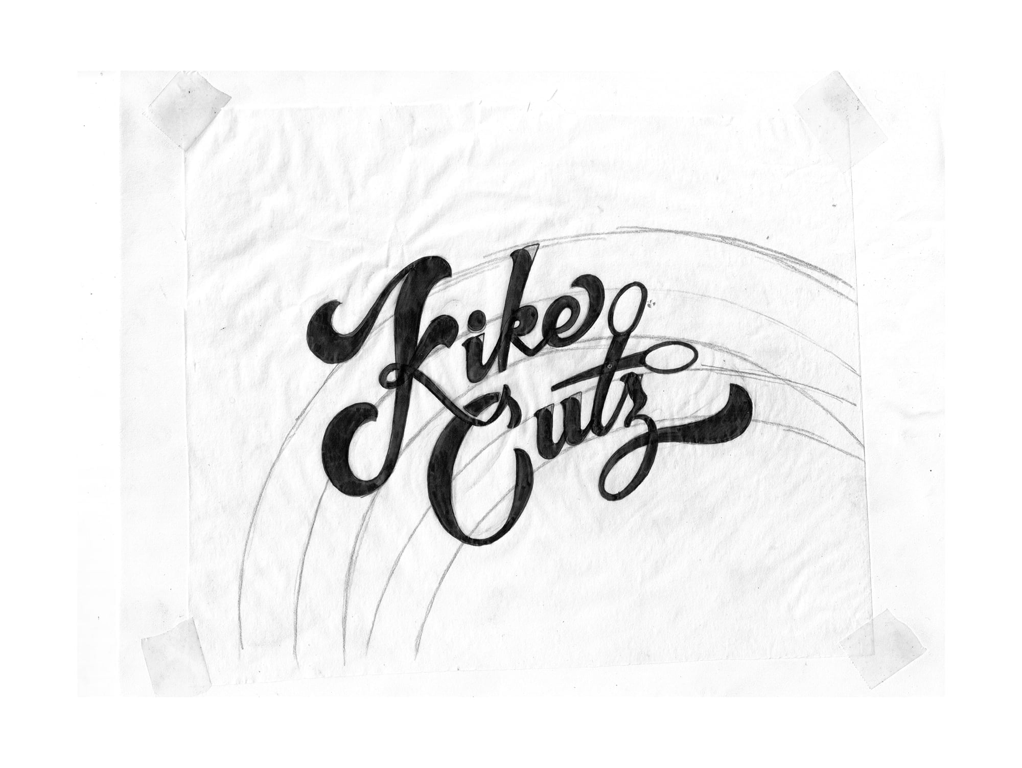 Refined pencil and ink sketch of Kike Cutz logo taped to surface with curved guideline arcs visible in the composition