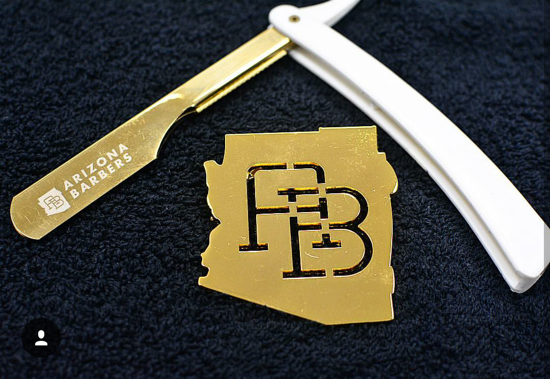 Gold Arizona Barbers lapel pin and branded collar stay displayed on dark fabric