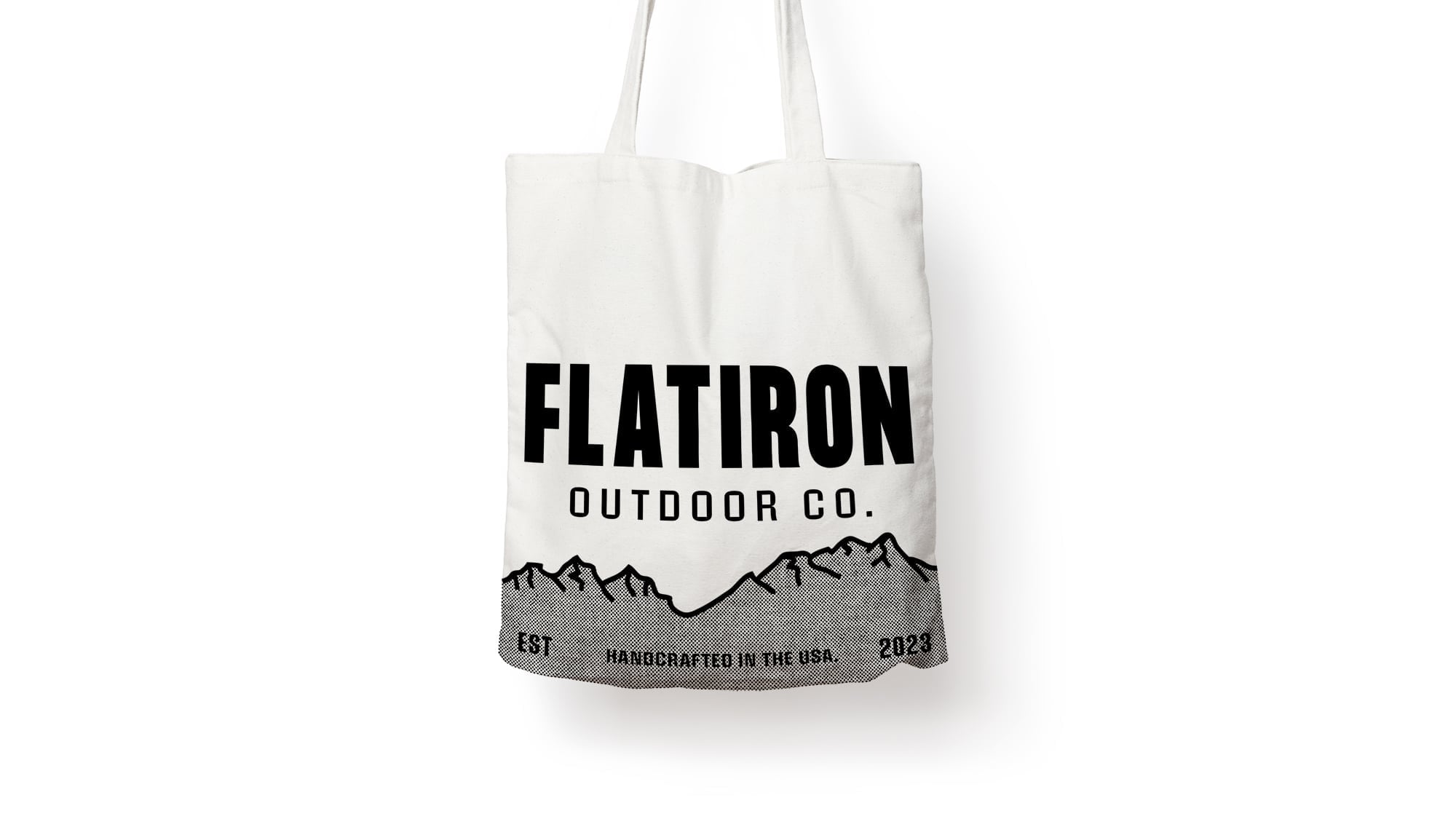 Natural white cotton canvas tote bag with bold black Flatiron Outdoor Co. wordmark, hand-drawn mountain range illustration, and halftone texture accent strip at bottom.