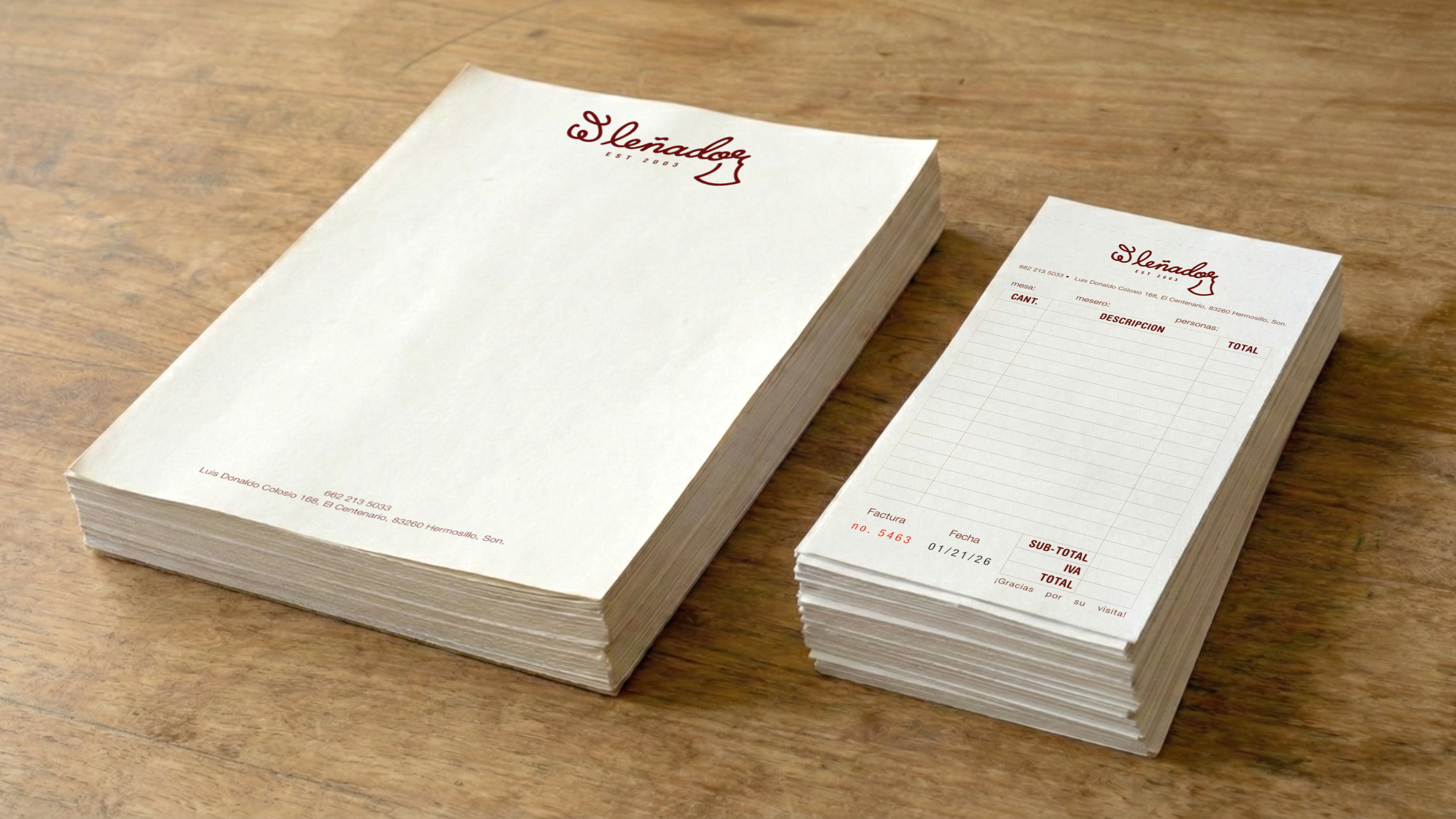 Stack of cream-colored branded letterhead and invoice pads on wooden surface featuring El Lenador maroon cursive logo header with contact details and ruled form layout for restaurant orders